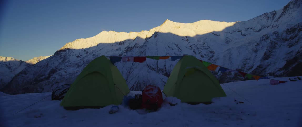 Two green tents with tibetan flags in the snow covered mountain peaks at morning