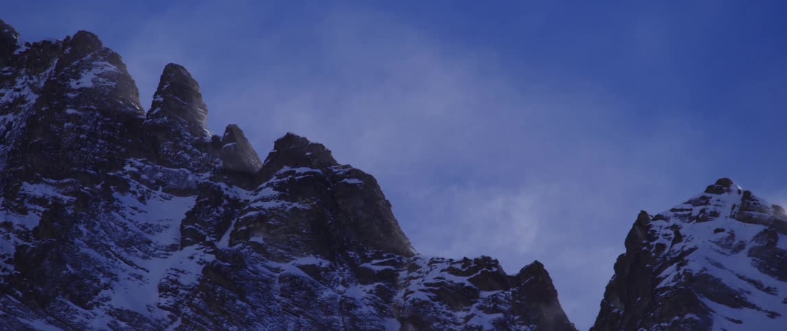 A snow covered mountain range with the sky and clouds in the background