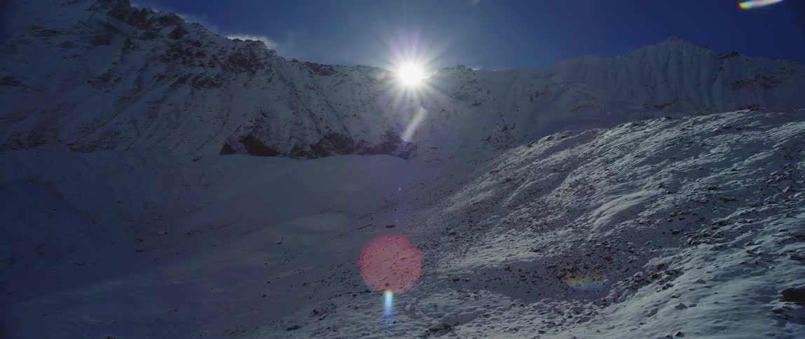Sun peaks over snow covered mountain under clear sky brightening part of shadowy slope