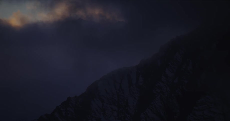 Thick clouds and fog shroud a mountain ridge in darkness