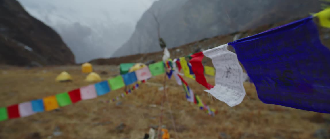 Fog covers mountains in background as tents sit on dried grass near lines decorated with banners