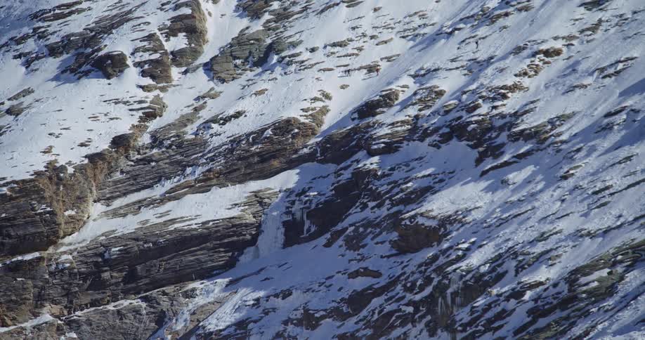 A distant view of three people hiking up a mountain covered with snow