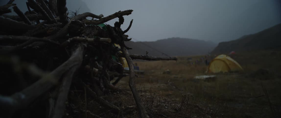 A bundle of sticks on the edge of a camp in a fog shrouded field on a snowy evening