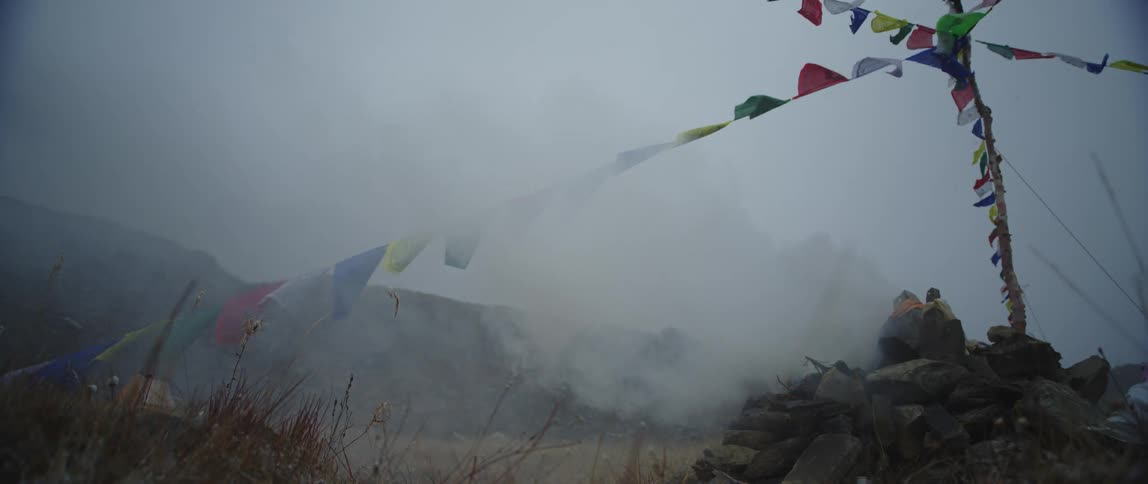 A pile of rocks with smoke coming out of it with the sky and clouds in the background