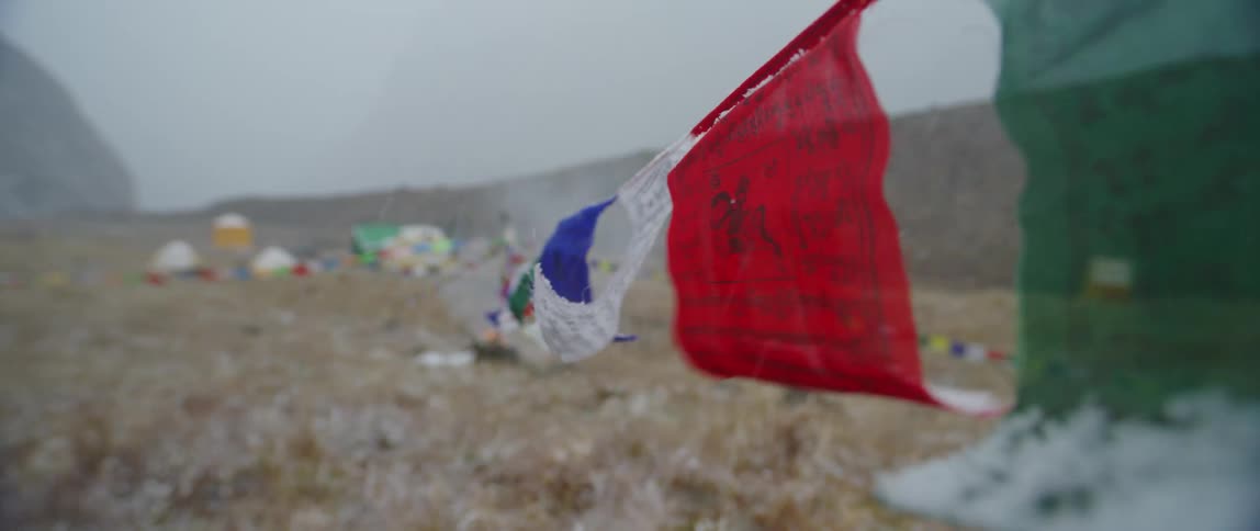 Colorful flags with text in a foreign language hang off a rope that leads to a house in a vast open field