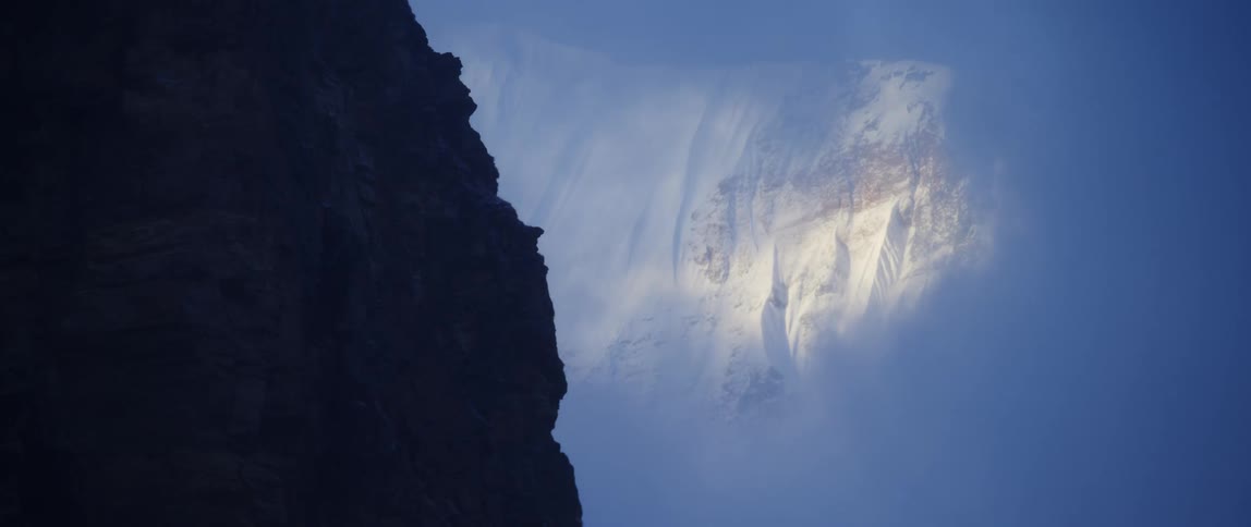Clouds float around a snowy mountain in the wilderness