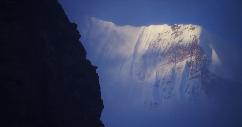 An enormous mountain is completely covered in snow as fog lingers in the air around it
