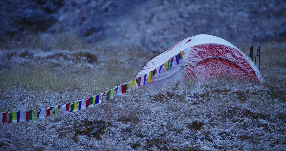A tent with a light dusting of snow sits at the bottom of a mountain