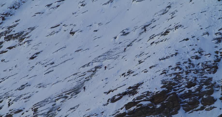 Hikers climbing up the side of a steep snow covered mountain in the wilderness