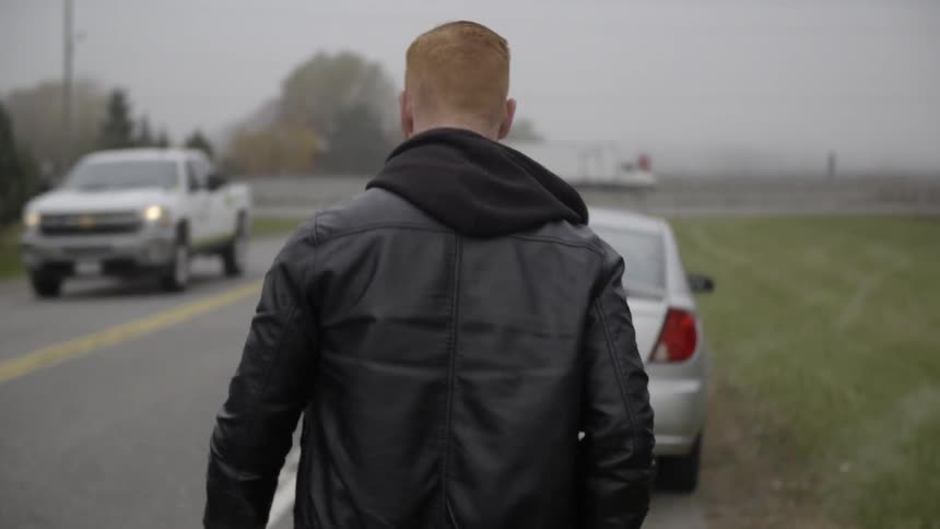 A man walks by the side of a road towards a car