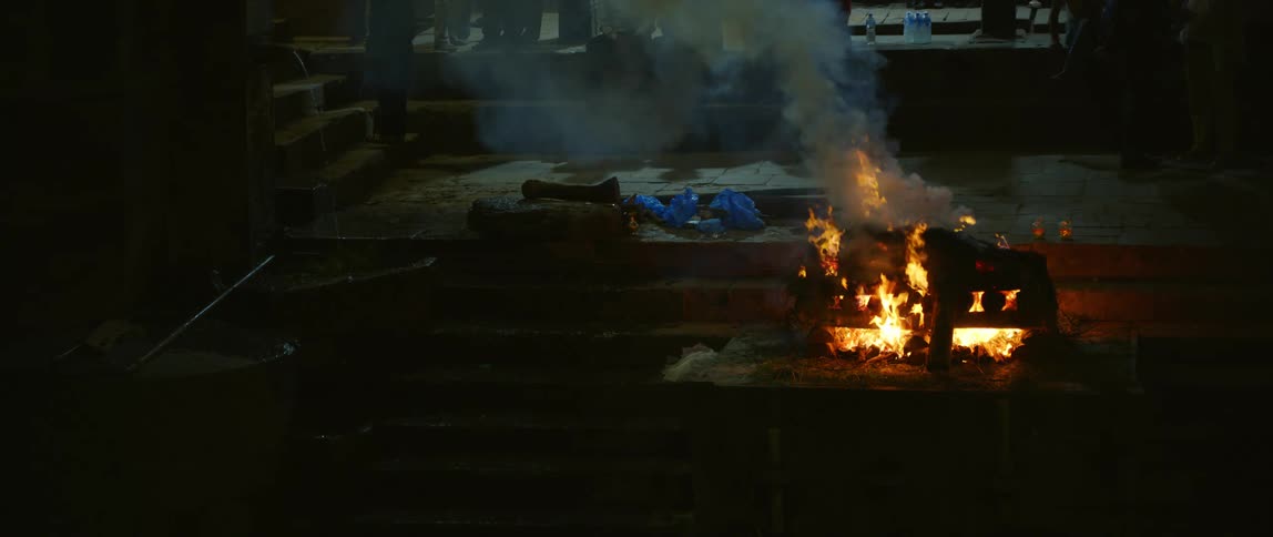 A fire burns as a woman walks past and people stand back