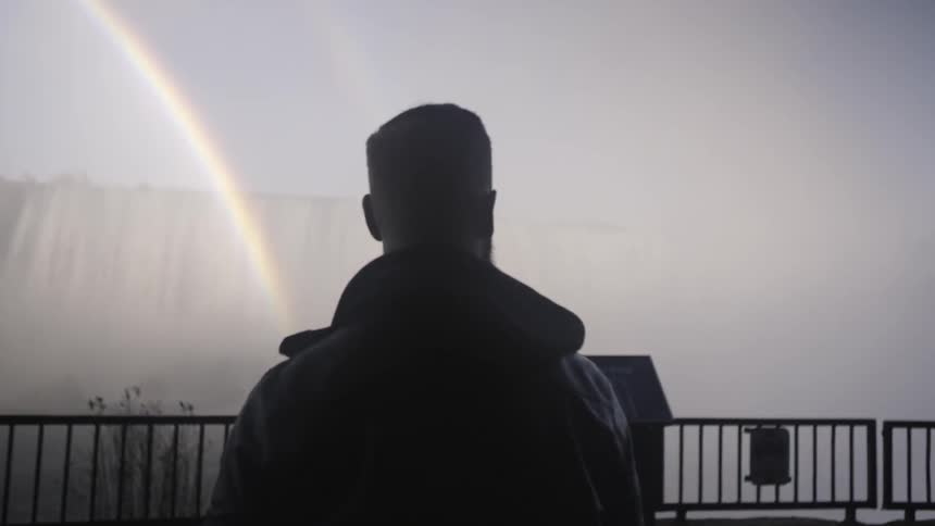 Man walks to edge of platform overlooking rainbow in front of niagara falls