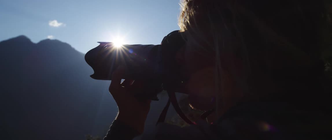 Woman taking photographs of the high mountains is silhouetted against the sun