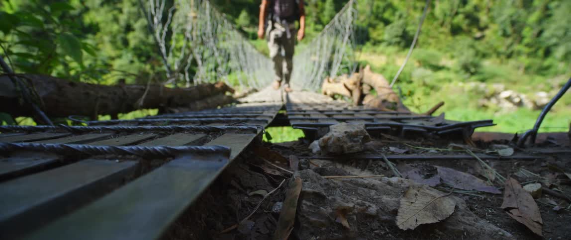 A man hiking walks across a suspension bridge