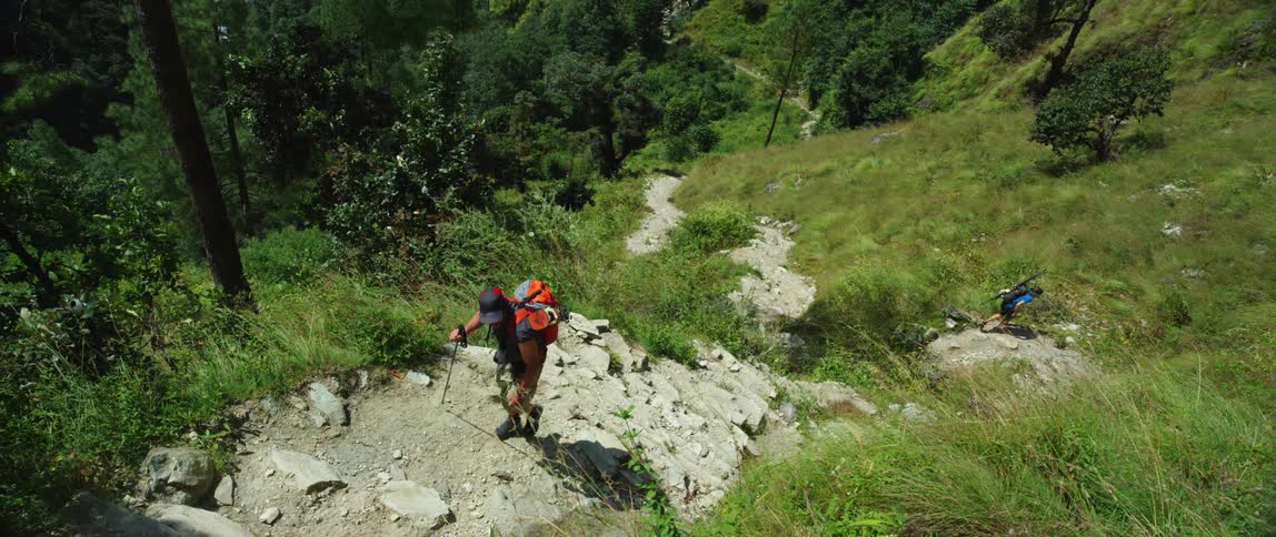 A hiker ascends a dilapidated stone staircase in the mountains as another hiker slowly follows behind him
