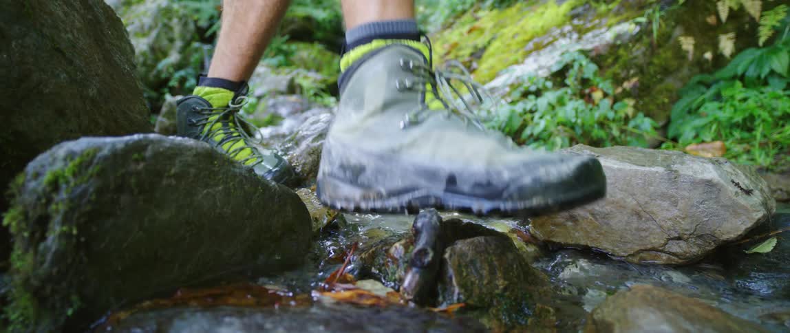 Bare legs in hiking boots step on rocks and splash in a stream