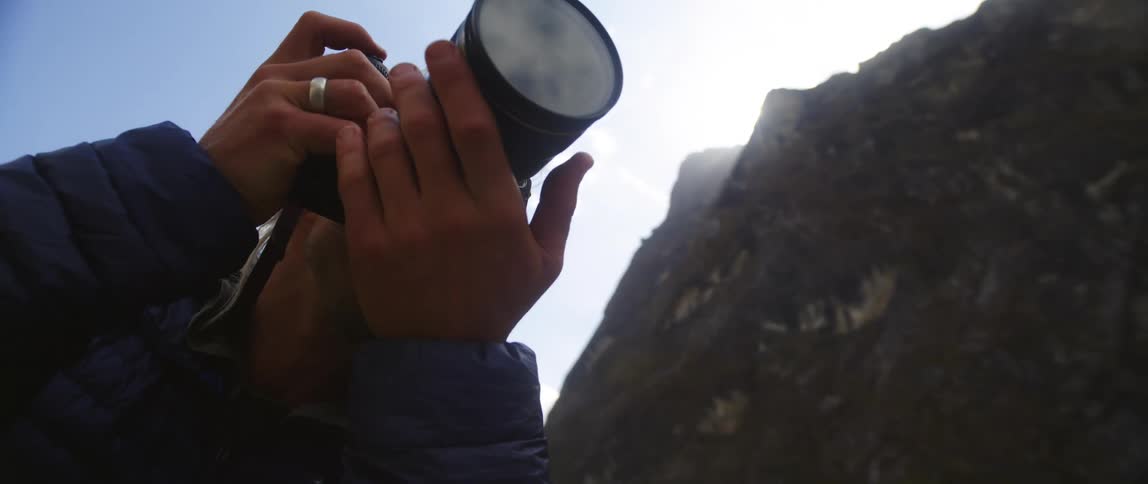 A photographer adjusts the lens of his camera while preparing to take a photo in the mountains on a sunny day