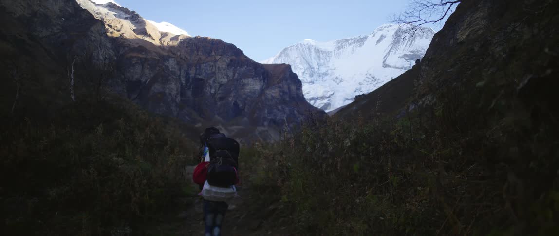 A group of hikers walk single file through the mountains on a sunny day