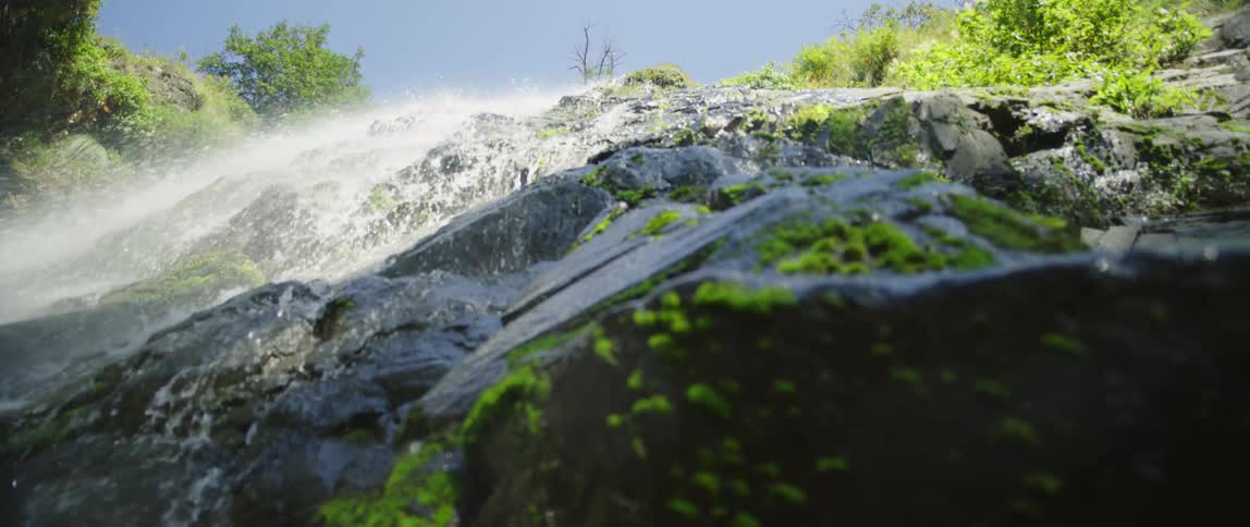 Water falls down a cliff covered in vegetation and stone on a sunny day