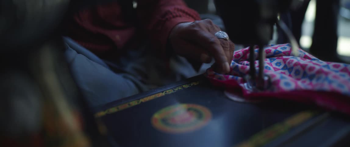 A person uses a sewing machine with one hand to sew a colorful fabric