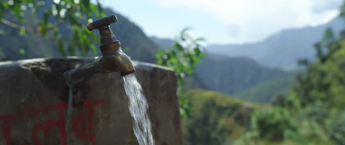 Clear fresh water flowing from a faucet near the mountains