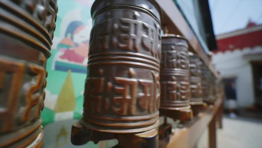 Metallic tibetan prayer wheel spinning near the wall of a temple