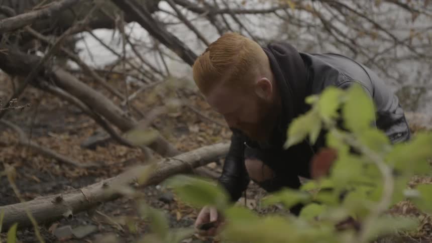 A man forages on the ground next to a lake