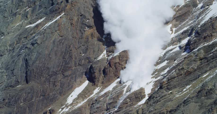 An avalanche cascades down a steep rocky mountains