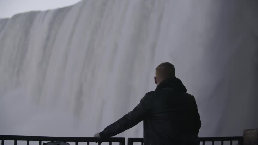 A man watches a large waterfall from a viewing deck