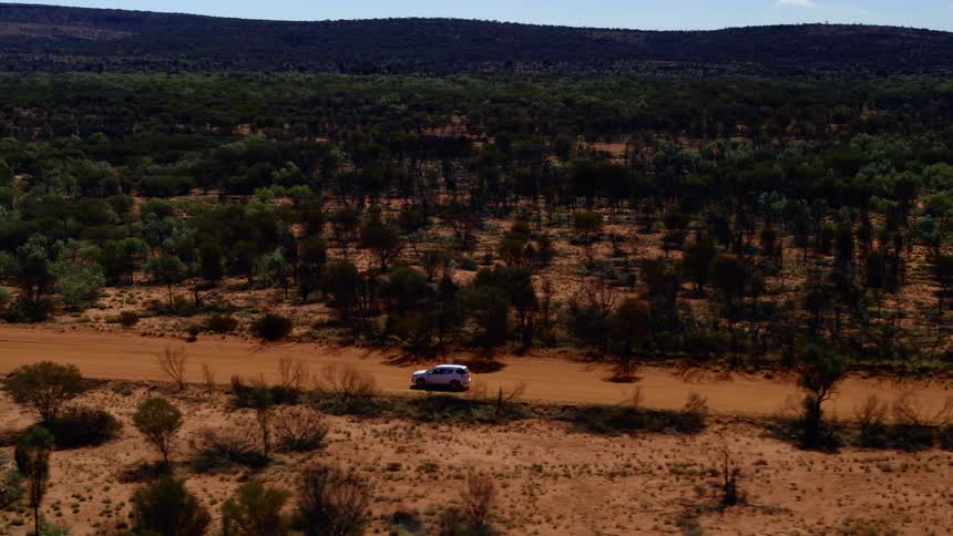 A car is driving in a rural area surrounded by trees