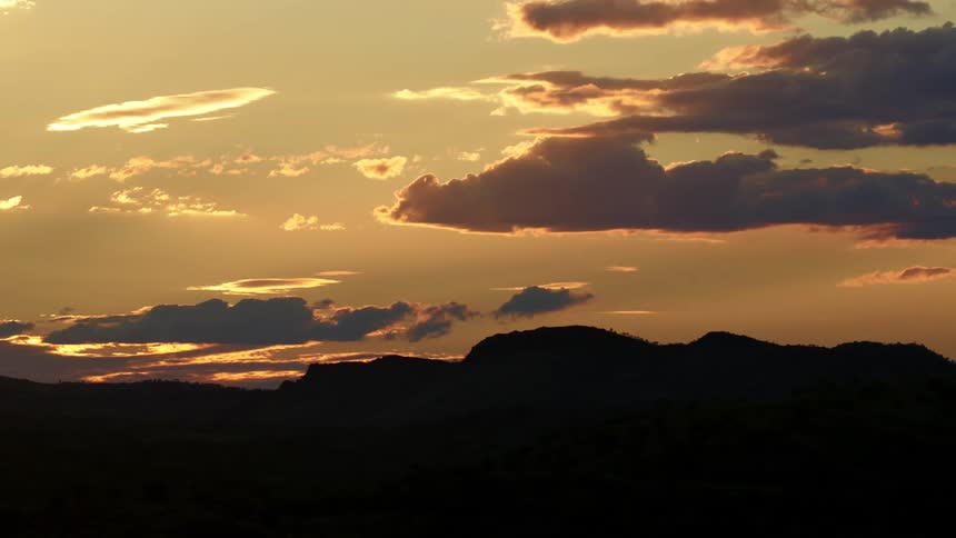 Clouds and a hill are silhouetted against the sunrise on the horizon
