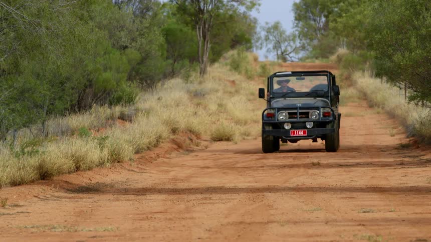 A man drives a jeep down a rural dirt road