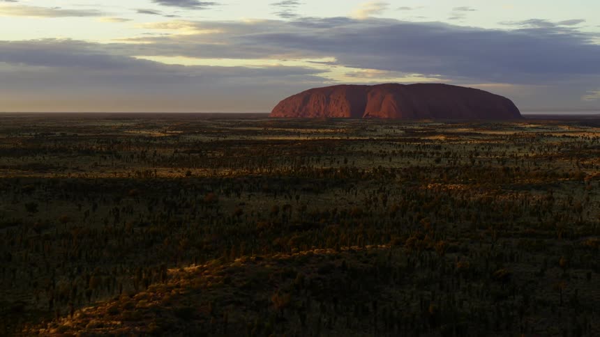 Uluru Ayers Rock in the middle of a field full of sharp brush and vegetation