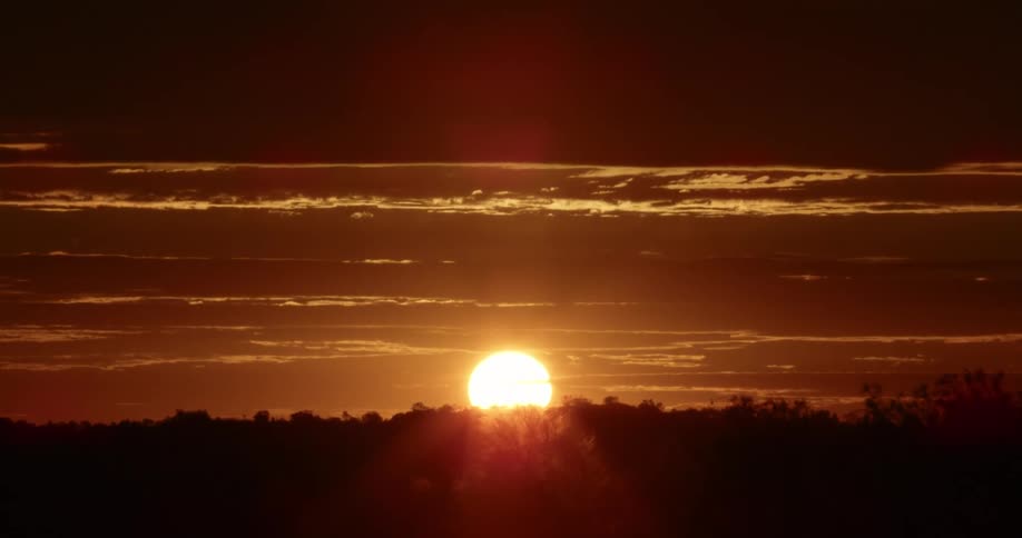 Clouds and a hill are silhouetted against the sunrise on the horizon