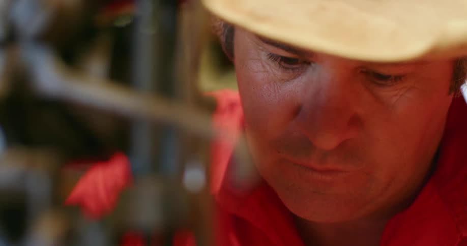 A worker wearing a red shirt and a hat working intently on machinery