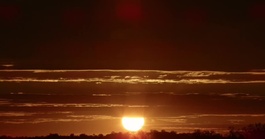 Clouds and a hill are silhouetted against the sunrise on the horizon