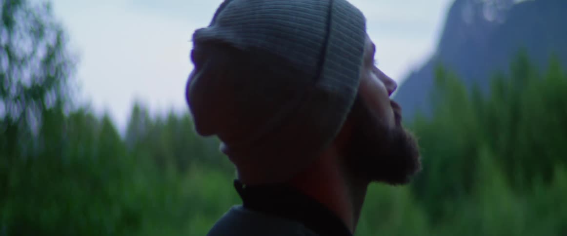 A man is standing in the forest while wearing a hat