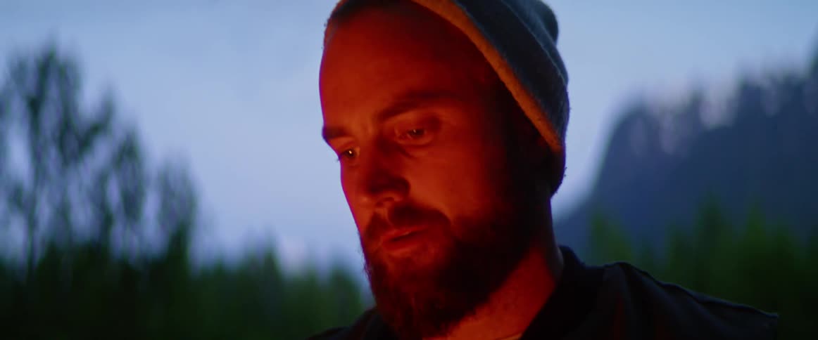 Mans face lit by firelight outdoors at dusk