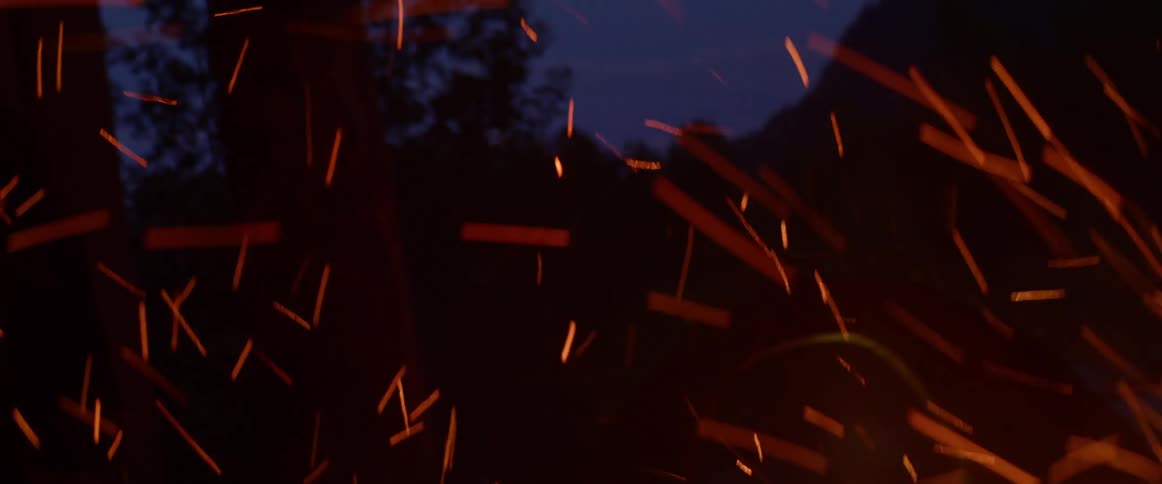 A man with a hat poking a bonfire with a stick