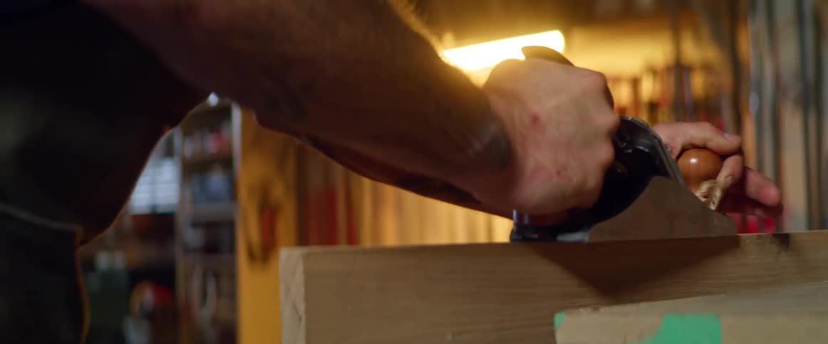 Man pushes planer across edge of wooden board in workshop