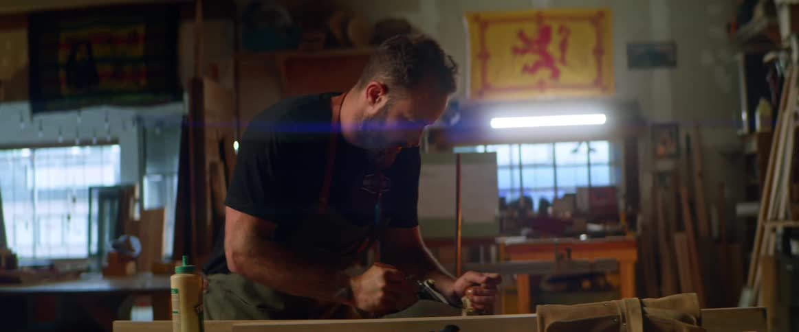 A man uses a power tool on a piece of wood in a large workshop