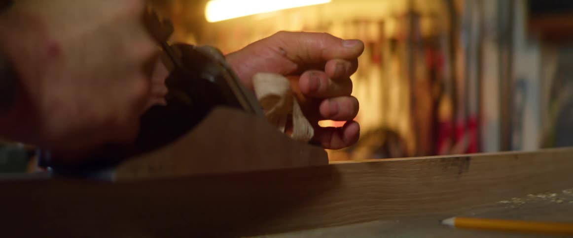 Man uses hand tool on wood in workshop