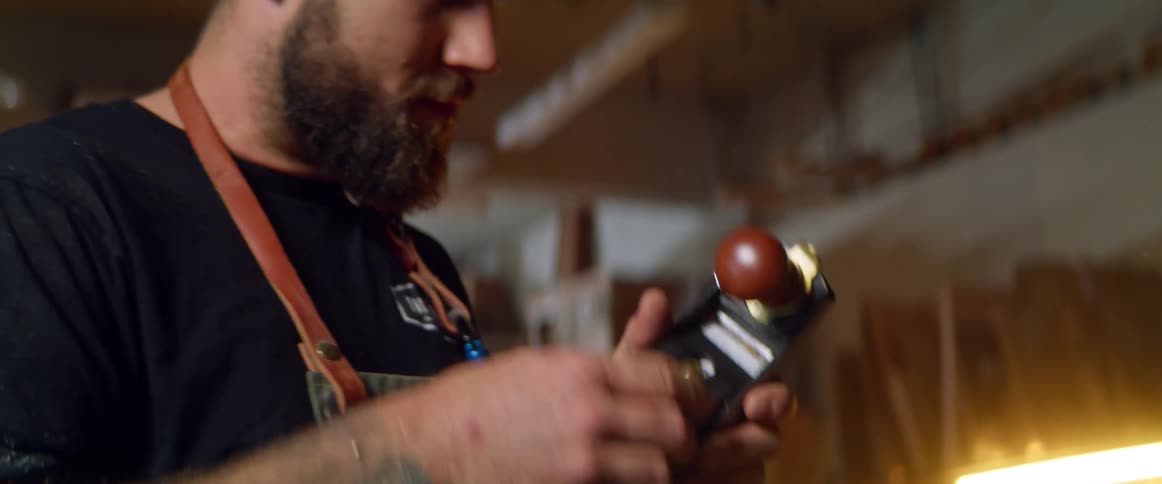 A man in his garage blows on a tool to clean dust out