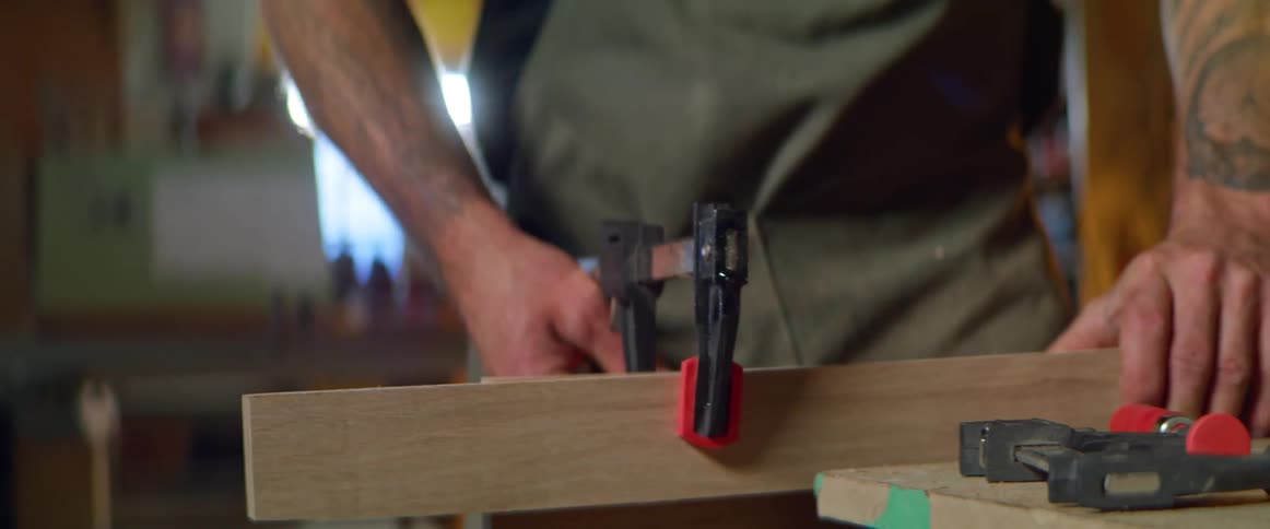 A man with a apron in a workshop tightening a vice on a piece of wood