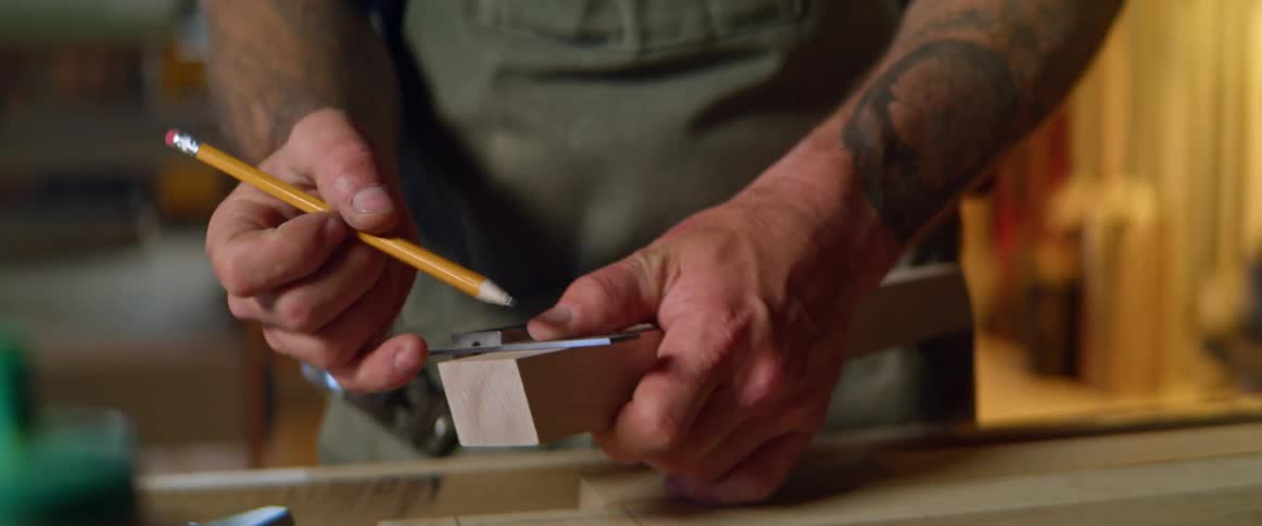 Man marks measurement on piece of wood in workshop