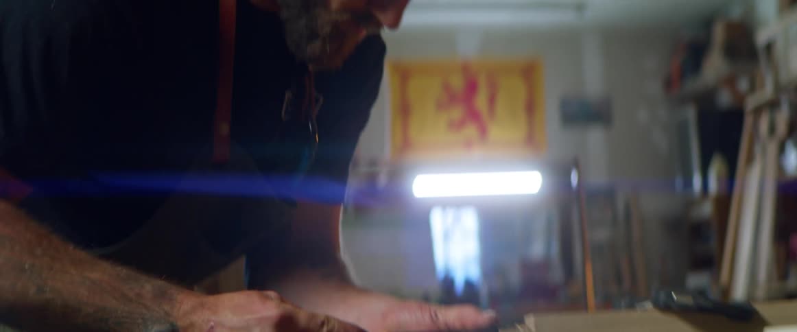 A man uses a chisel to chip away pieces of a wooden board