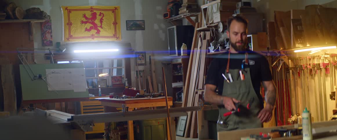 A man wearing a work apron is working with wood in a workshop