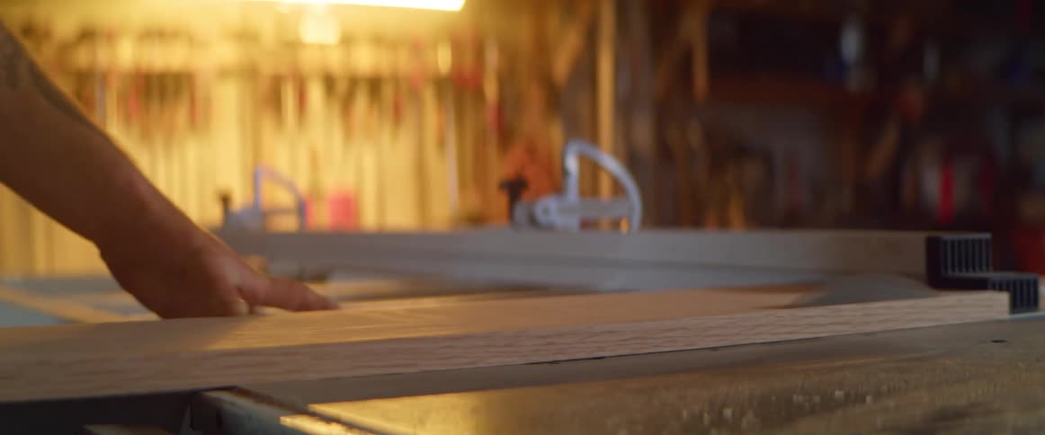 A man uses a table saw to cut a wooden plank