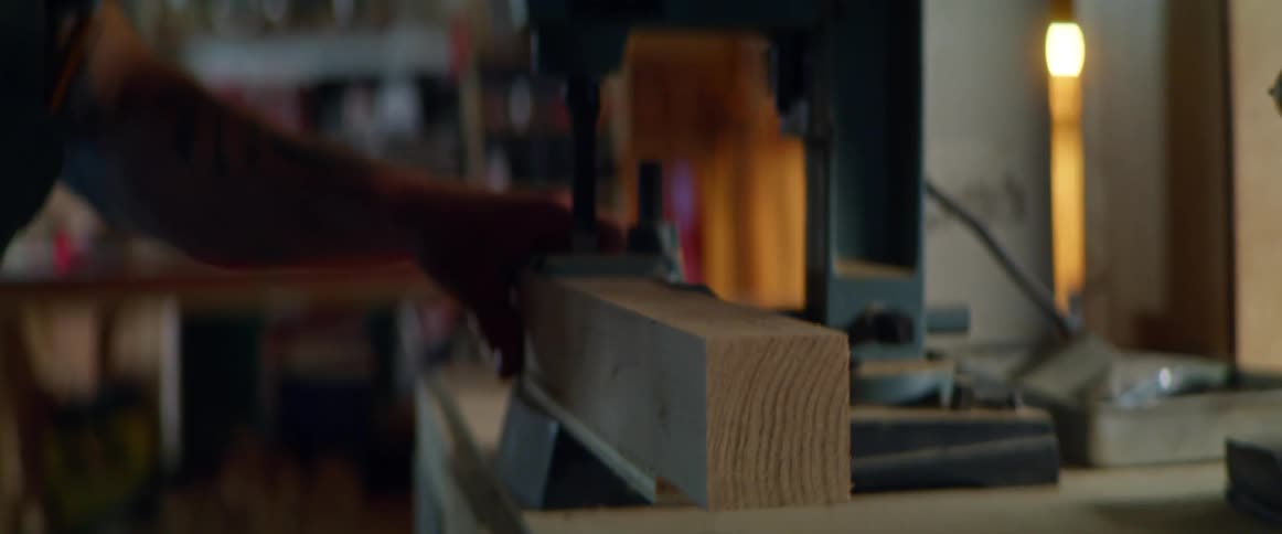 A man is working inside a workshop preparing to drill a hole into lumber
