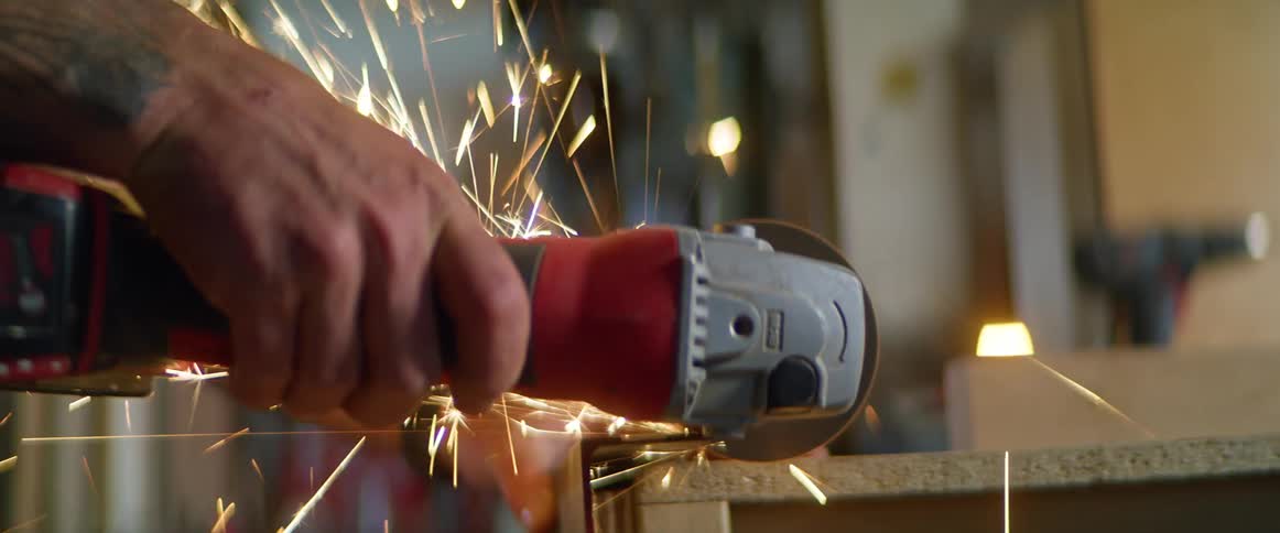 A man with overalls in a workshop using a grinding tool to grind metal with sparks
